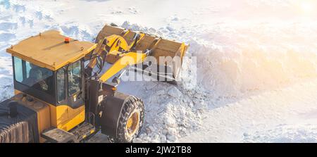 A large orange tractor removes snow from the road and clears the sidewalk. Cleaning and clearing roads in the city from snow in winter. Snow removal a Stock Photo