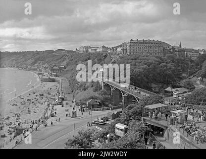 A view c. 1960 of the South Bay, Scarborough, North Yorkshire, England, UK. Centre is The Cliff Bridge, previously known as the Spa Bridge, a footbridge spanning the valley from St Nicholas Cliff to The Spa. It was completed in 1827. In the foreground is the St Nicholas Cliff Lift. This funicular was one of five in Scarborough. It opened in 1929, linking Scarborough’s Grand Hotel at the top with the town’s aquarium, Gala Land, at the base. This lift closed in 2007. Beachside, centre left, is The Spa, an entertainment centre. Centre right is The Esplanade hotel – a vintage 1950s/60s photograph. Stock Photo