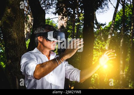 The young man is using a virtual reality viewer in the park. The handsome businessman is working with a virtual reality viewer outdoors. Stock Photo