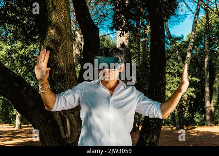 The young man is using a virtual reality viewer in the park. The handsome businessman is working with a virtual reality viewer outdoors. Stock Photo