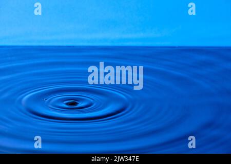 Splash drop of water with diverging water circles, on blue background Stock Photo