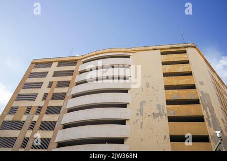 Low angle view of the curved facade of an empty, multi-level concrete parking garage building against a bright blue sky, Spain. Stock Photo
