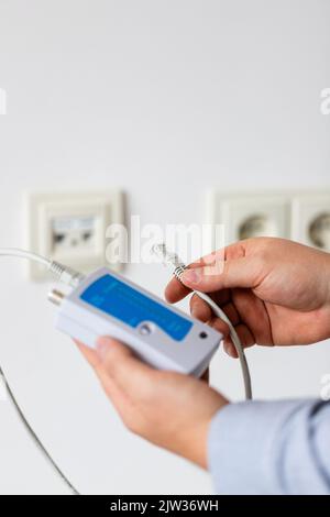 Network cable tester. Testing structured cabling using qualified cable performance tester. Close up of network cable tester with UTP cable in hands of Stock Photo
