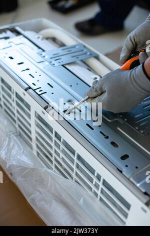 Male installation service worker or repairman installs or repairs air conditioner indoors. Close up of man in work gloves using screwdriver to disasse Stock Photo