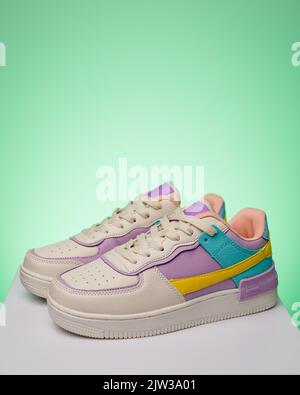 Pair of fashionable bright sports shoes for teens standing on white podium on light green background. Side view of white sneakers with turquoise and p Stock Photo