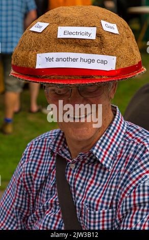 Bridport, Dorset UK. 3rd September 2022. A variety of style and quirky hats made and worn by humans and dogs at the Bridport Hat Festival in Dorset. Senior man wearing cap with stickers on Yet another huge cap, gas and electricity after the recent hike in energy bills. Credit: Carolyn Jenkins/Alamy Live News Stock Photo