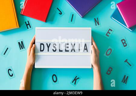 Dyslexia awareness, help children with reading, learning difficulties concept. Kid hand holding lightbox with DYSLEXIA word. Colorful books and Stock Photo