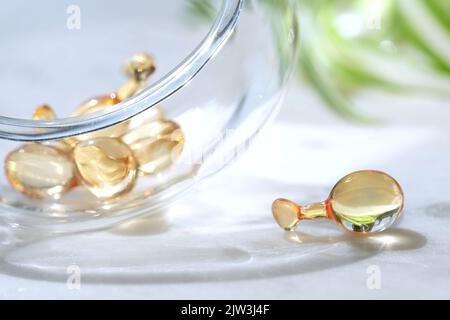 Serum capsules for healthy skin. Blurred background, glass jar with the capsules and green palm leaf Stock Photo