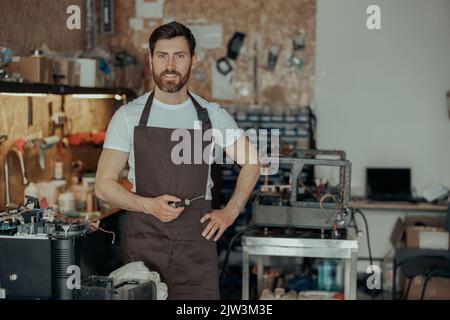 Repairman with a screwdriver standing on background of own workshop of coffee machines Stock Photo