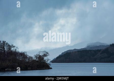 Lovely Winter landscape image of view along Loch Lomond towards snowcapped mountain range in distance during blue hour Stock Photo