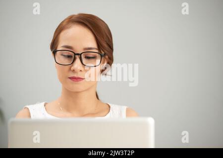 Beautiful young Asian business lady working on laptop, isolated on light grey Stock Photo