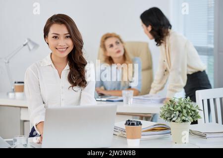Portrait of pretty young Vietnamese business lady working on laptop in office Stock Photo