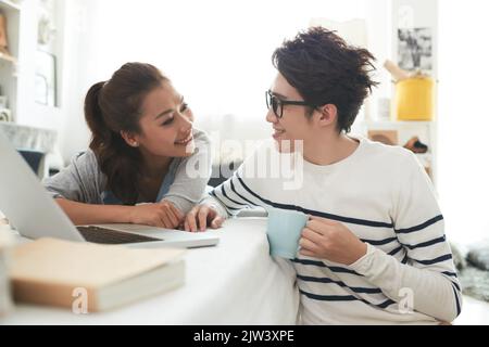 Cheerful young Vietnamese couple drinking coffee and watching something on laptop Stock Photo