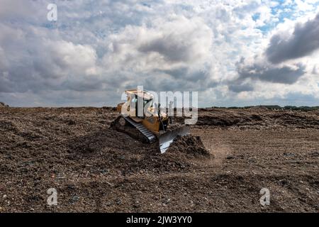 A Bulldozer machine moving waste and household garbage on a large landfill heap Stock Photo