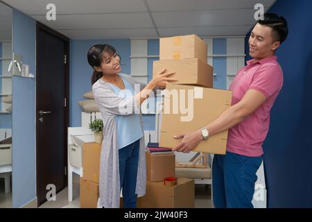 Young Asian couple packing carton boxes with household stuff and smiling happily while moving in new apartment Stock Photo