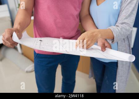 Unrecognizable couple holding blueprint of their new home, discussing maintenance and furniture arrangement Stock Photo