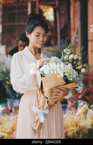 Smiling young woman looking at big bouquet of pastel color flowers in her hands Stock Photo