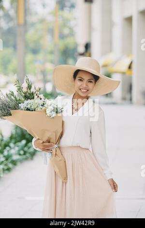 Lovely pretty smiling woman in light clothes holding bouquet of flowers Stock Photo