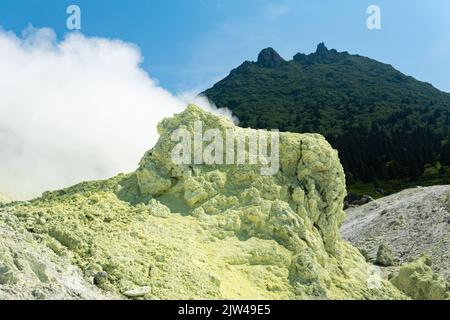 bright smoking fumarole with sulfur deposits against the background of the Mendeleev volcano peak on the island of Kunashir Stock Photo