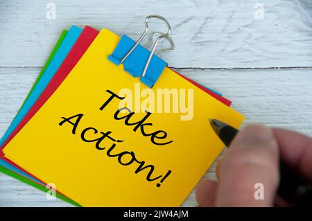 Motivational and inspirational quotes text on notepad - Take Action. With hand holding pen. Stock Photo