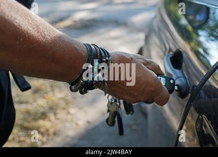 Man opening his car with a car key. He wears a lot of leather bracelets Stock Photo