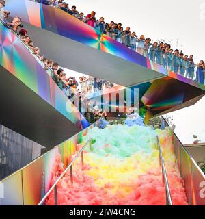 London, UK. 03rd Aug, 2022. People interact with 'Island of Foam: Version XVIII', a colourful, constantly changing foam installation. The installation is a UK premiere from German artist Stephanie Lüning (who is operating the 'foam cannon' at the top of the stairs), transforming Greenwich Peninsula with mountains of rainbow coloured foam. Credit: Imageplotter/Alamy Live News Stock Photo