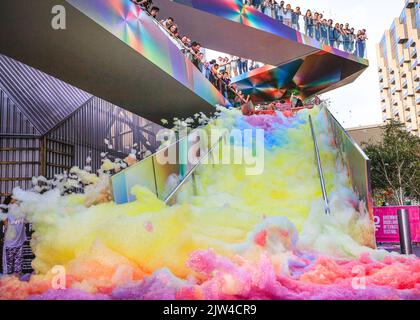 London, UK. 03rd Aug, 2022. People interact with 'Island of Foam: Version XVIII', a colourful, constantly changing foam installation. The installation is a UK premiere from German artist Stephanie Lüning (who is operating the 'foam cannon' at the top of the stairs), transforming Greenwich Peninsula with mountains of rainbow coloured foam. Credit: Imageplotter/Alamy Live News Stock Photo