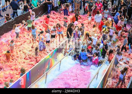 London, UK. 03rd Aug, 2022. People interact with 'Island of Foam: Version XVIII', a colourful, constantly changing foam installation. The installation is a UK premiere from German artist Stephanie Lüning (who is operating the 'foam cannon' at the top of the stairs), transforming Greenwich Peninsula with mountains of rainbow coloured foam. Credit: Imageplotter/Alamy Live News Stock Photo