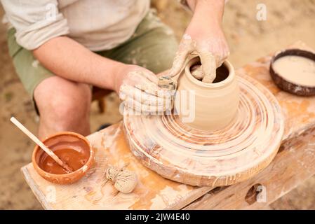 man master in light linen shirt makes clay product on mechanical potter's wheel Stock Photo