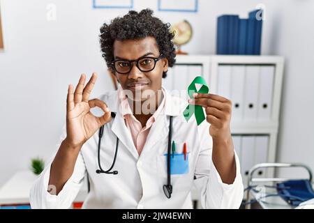African doctor man holding support green ribbon doing ok sign with fingers, smiling friendly gesturing excellent symbol Stock Photo
