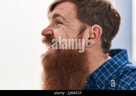 Young redhead man using deafness aid machine sitting on sofa at home Stock Photo