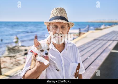 Senior man wearing summer hat hugging chihuahua at seaside Stock Photo