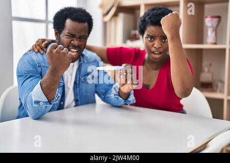 Young african american couple holding pregnancy test result annoyed and frustrated shouting with anger, yelling crazy with anger and hand raised Stock Photo