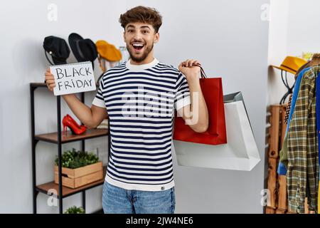 Young arab man customer holding shopping bags and black friday banner at clothing store Stock Photo