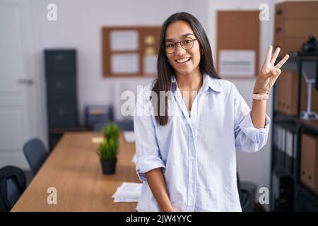 Young hispanic woman at the office showing and pointing up with fingers number three while smiling confident and happy. Stock Photo