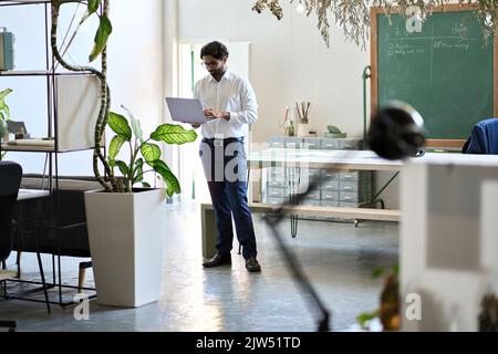 Young indian business man manager working on laptop standing in office space. Stock Photo