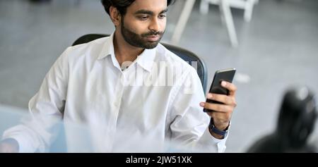 Busy indian business man using cell phone at workplace in office. Stock Photo
