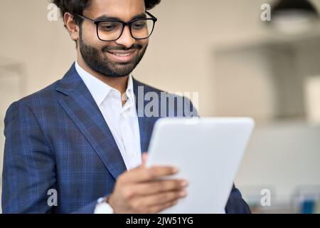 Smiling young indian business manager wearing suit using digital tablet. Stock Photo