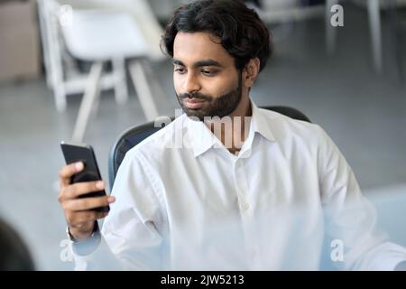 Young indian businessman using mobile phone apps at work in office. Stock Photo