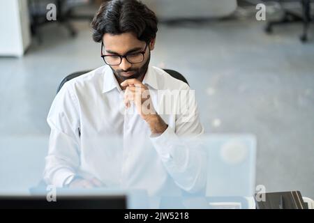 Busy serious indian business man analyzing market data, looking at computer. Stock Photo