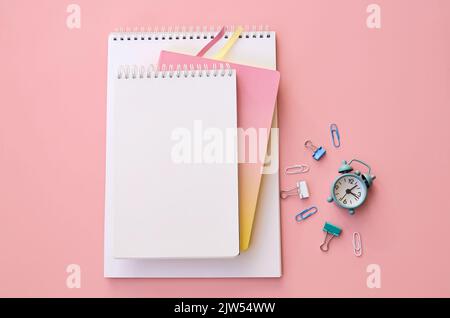 Small alarm clock and school supplies on pink background, flat lay, top view. Stock Photo
