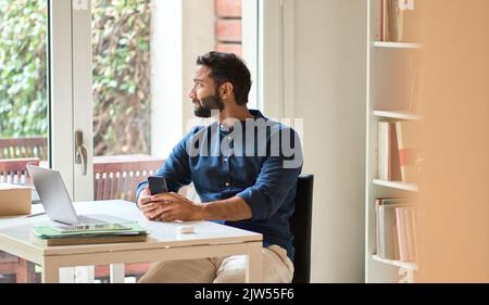 Indian professional business man holding smartphone working at home. Stock Photo
