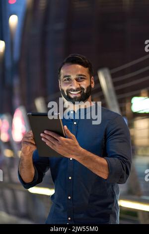 Happy indian business man using digital tablet outdoor in night city, vertical. Stock Photo