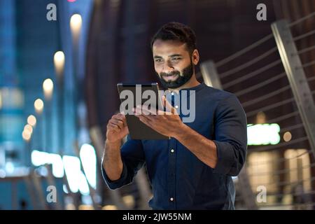 Professional indian business man using digital tablet outdoors in night city. Stock Photo
