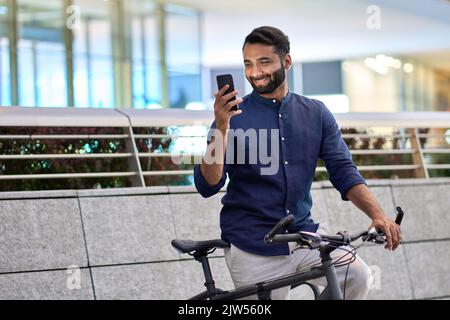 Indian man using phone using bike rental app renting bicycle in city park. Stock Photo