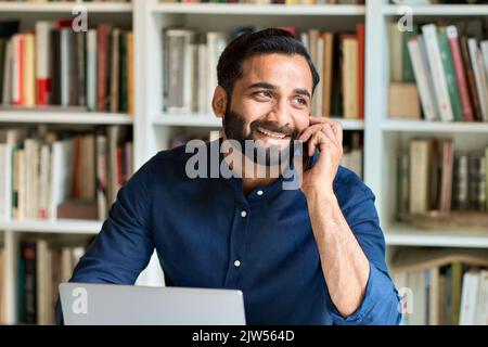 Happy indian business man working in office talking on phone making call. Stock Photo