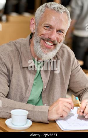 Happy old man professor writing in notebook sitting at table. Vertical portrait Stock Photo