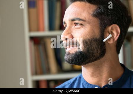 Smiling indian man wearing earbud listening music or podcast. Close up Stock Photo