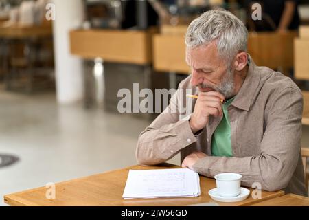 Thoughtful old business man writing in notebook taking notes and thinking. Stock Photo