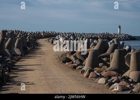 A trail leading to a lighthouse with wave breakers on the side during the day Stock Photo